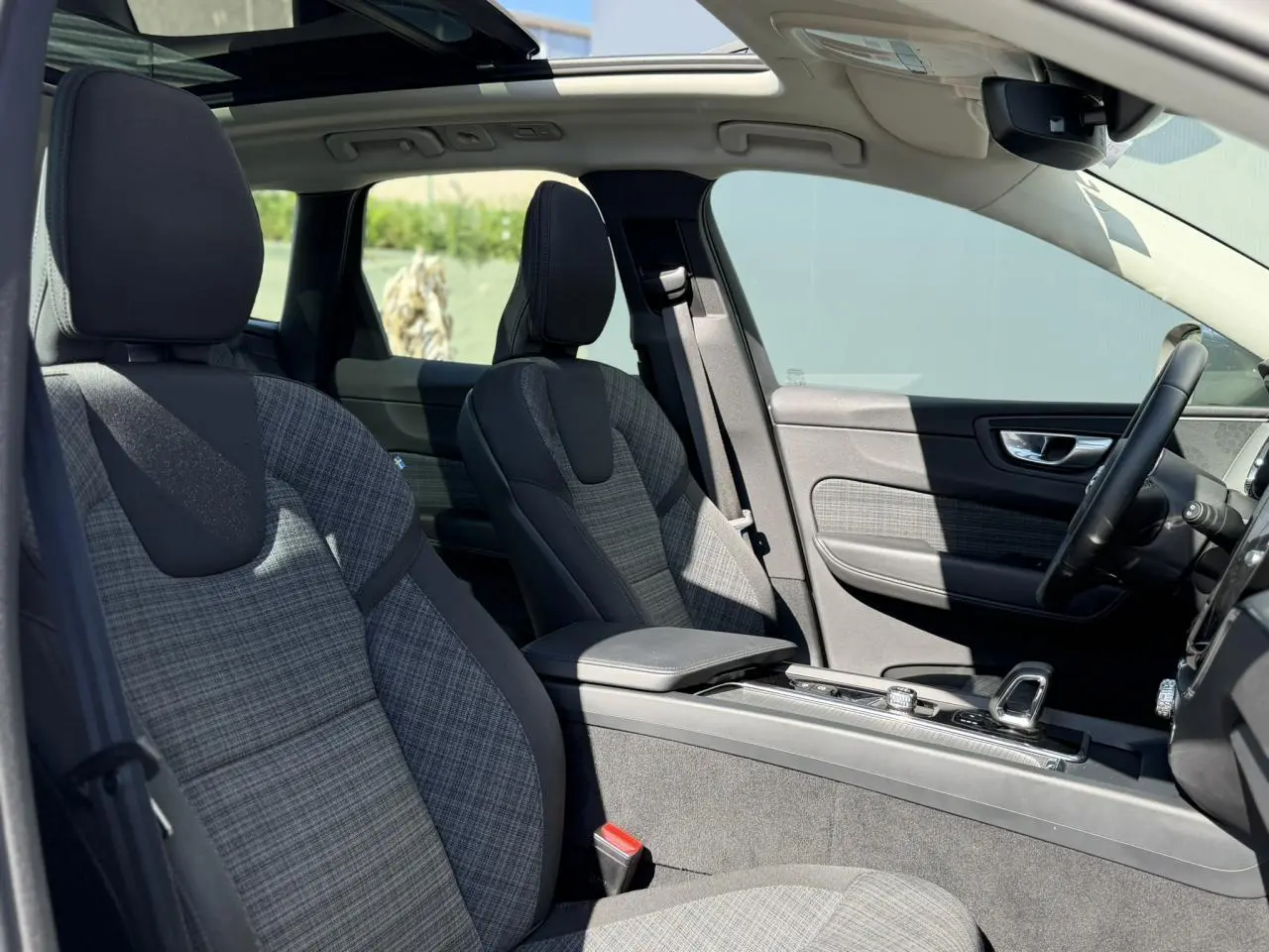Intérieur avant du Volvo XC60 T6 AWD PHEV 2024, sièges en tissu gris à motif, toit ouvrant panoramique visible.