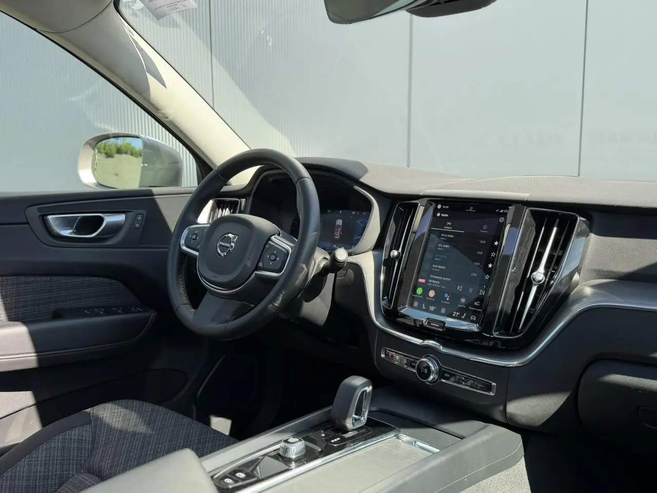 Vue intérieure côté conducteur du Volvo XC60 2024, avec tableau de bord noir et écran tactile vertical.