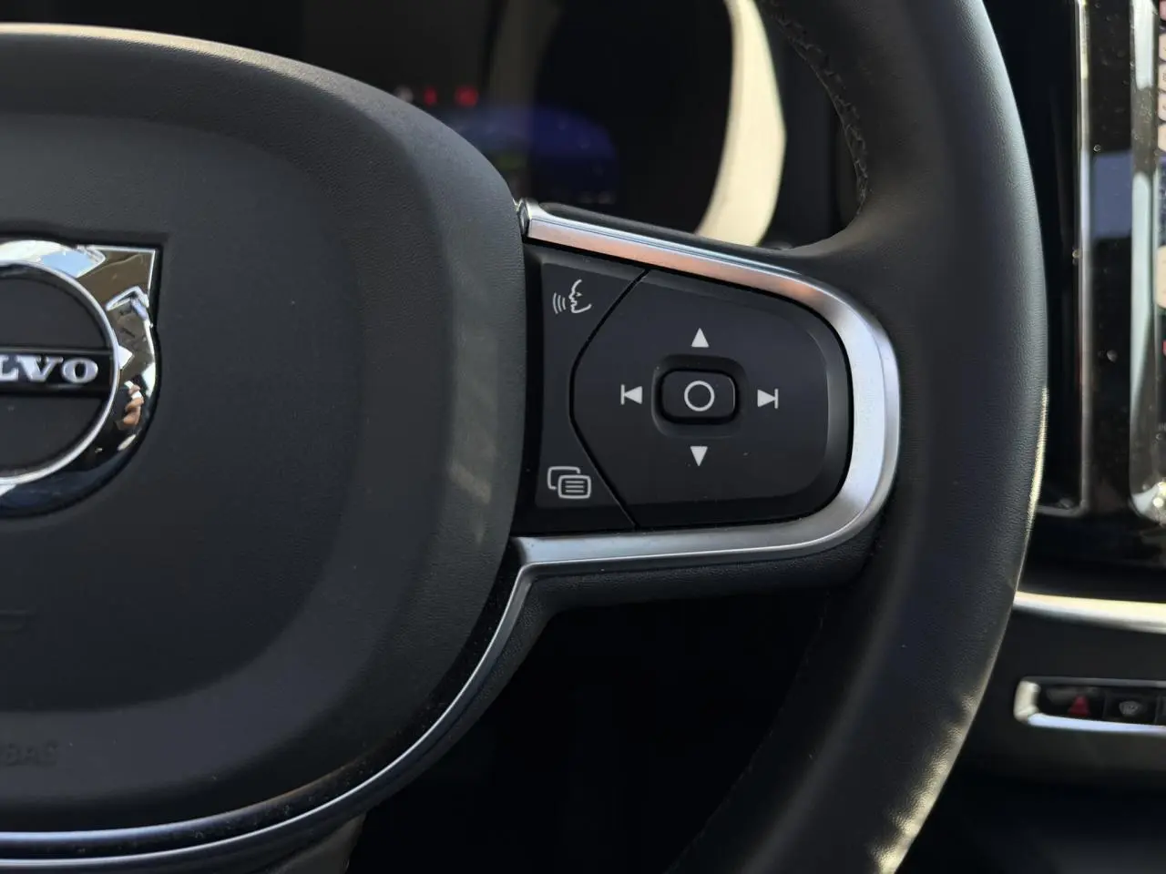 Gros plan sur le côté droit du volant noir simili-cuir du Volvo XC60 2024 avec commandes intégrées et logo chromé.