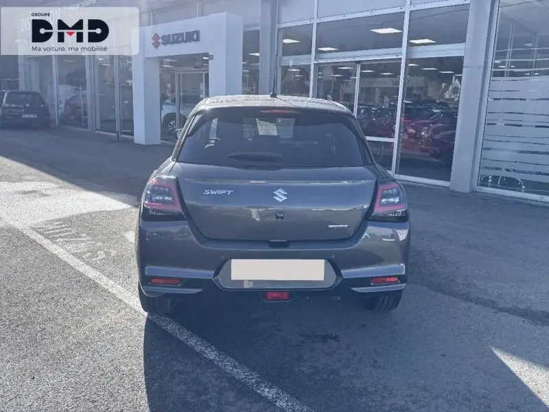 Vue arrière d'une Suzuki Swift 1.2 Hybrid 83ch Privilège en Mineral Gray Metal, stationnée devant un showroom Suzuki.