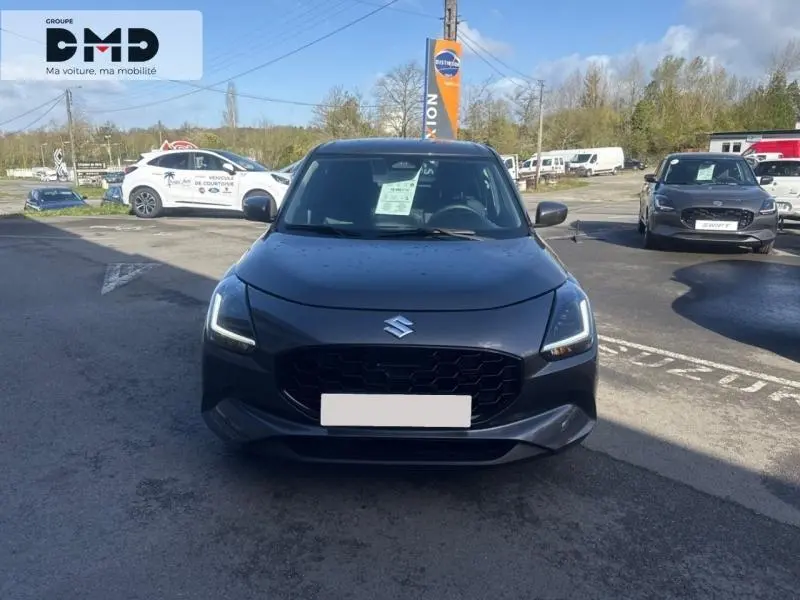 Vue frontale d'une Suzuki Swift 1.2 Hybrid 83ch Privilège gris Mineral Gray Metal avec phares LED allumés sur parking.