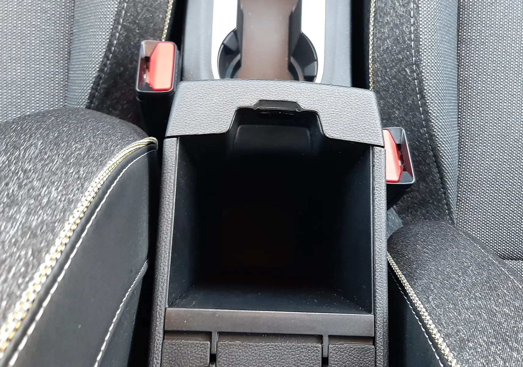 Vue plongeante sur le rangement central noir et les sièges tissu gris du Renault Captur 2024 avec surpiqûres jaunes.