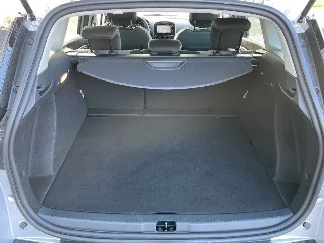 Coffre ouvert vu de l'arrière d'une Renault Clio IV Estate gris titanium, montrant l'espace de chargement et l'intérieur des sièges.