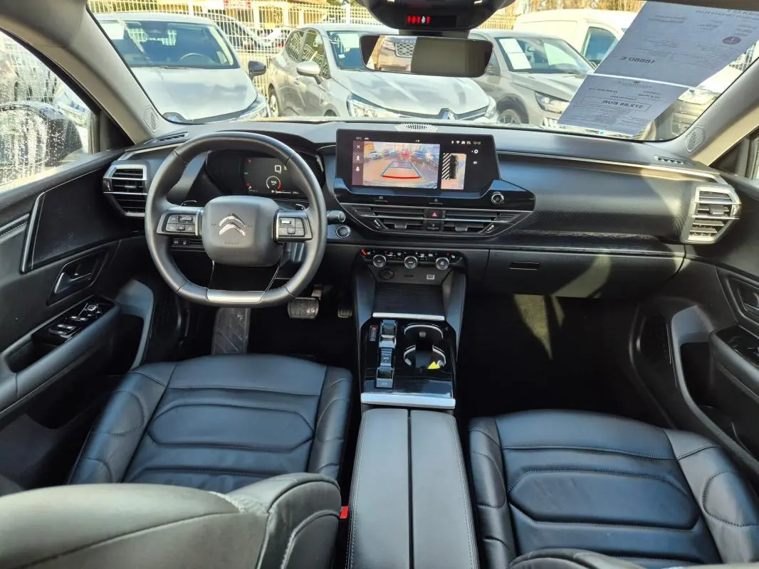 Vue intérieure avant de la Citroën C5 X 2024 noire, montrant le tableau de bord avec écran tactile et volant multifonction cuir.