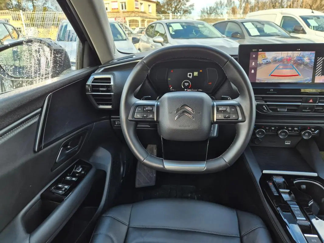 Vue intérieure centrée sur le volant cuir de la Citroën C5 X noire, avec tableau de bord digital et écran de caméra de recul.