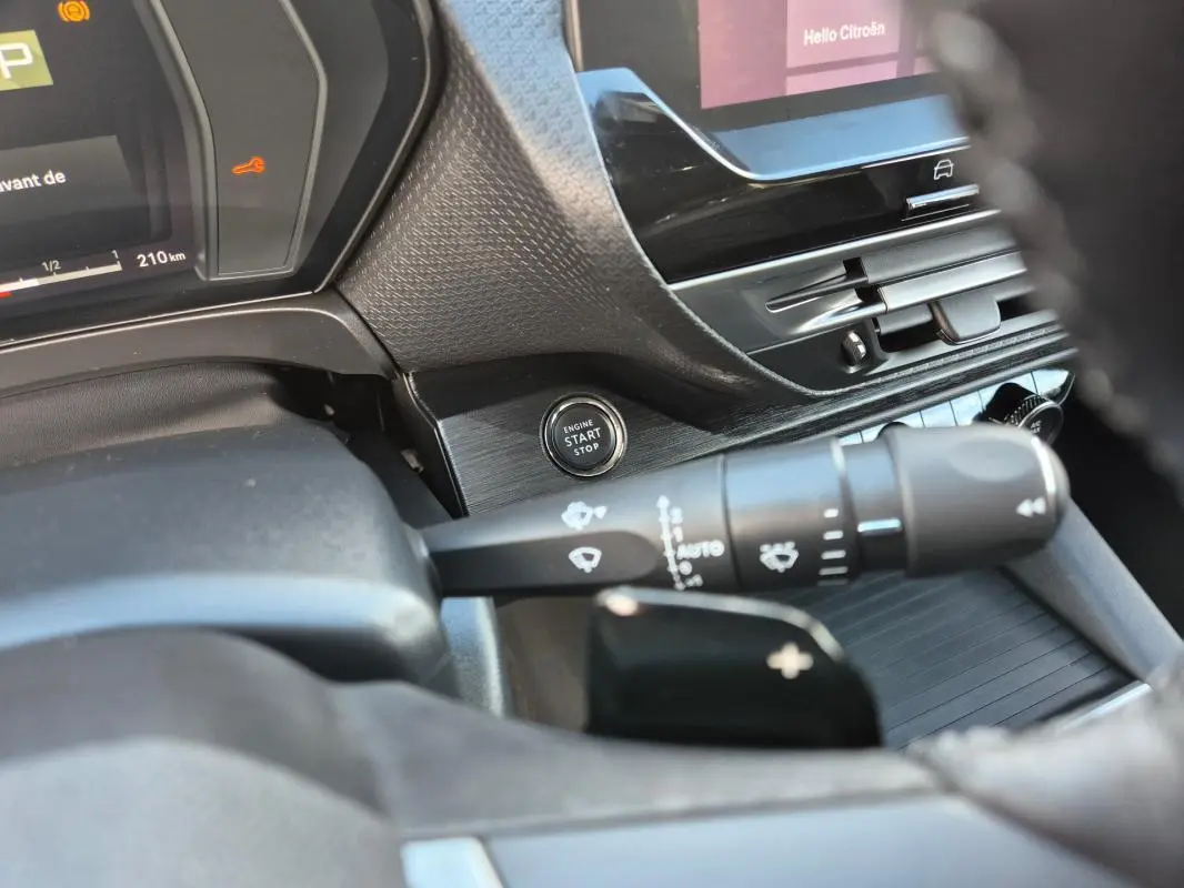 Détail intérieur du Citroën C5 X 2024 noir, bouton start/stop et commandes de phares sur le côté gauche du volant cuir.