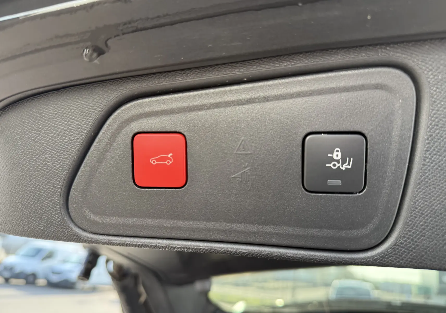 Gros plan sur les boutons de commande du hayon électrique du Peugeot 3008 gris, avec bouton rouge d'ouverture et bouton noir de verrouillage.