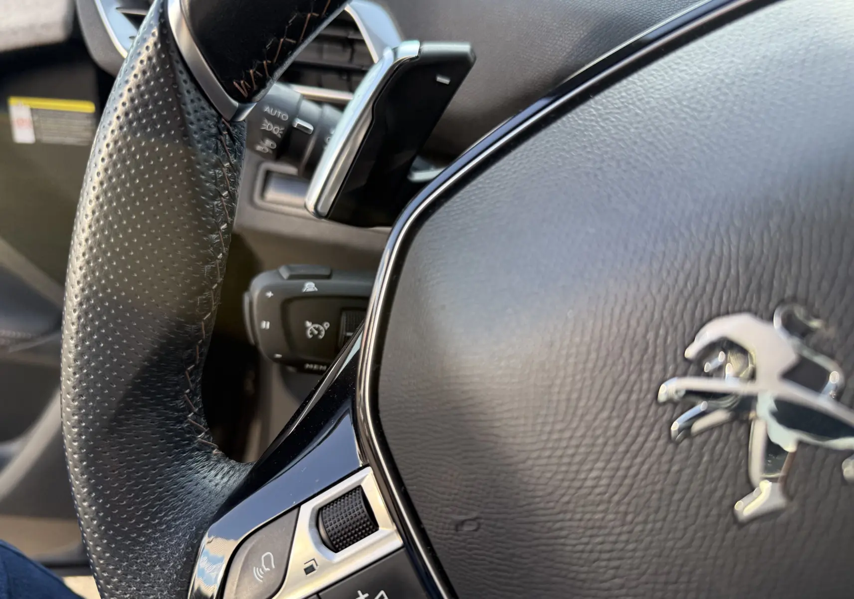 Gros plan sur le volant en cuir noir avec commandes intégrées du Peugeot 3008 gris, version 2022, côté gauche.