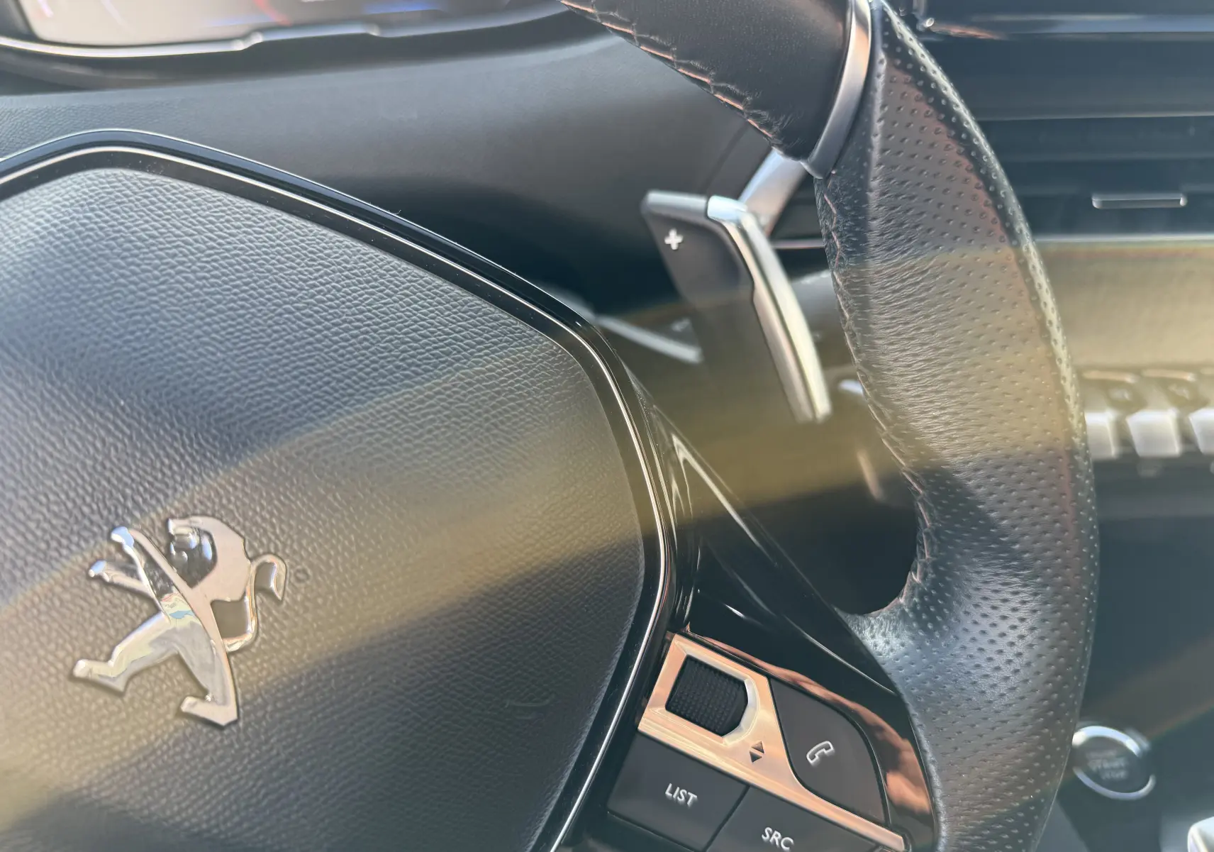 Gros plan sur le volant en cuir perforé du Peugeot 3008 gris, avec commandes intégrées et logo lion argenté.