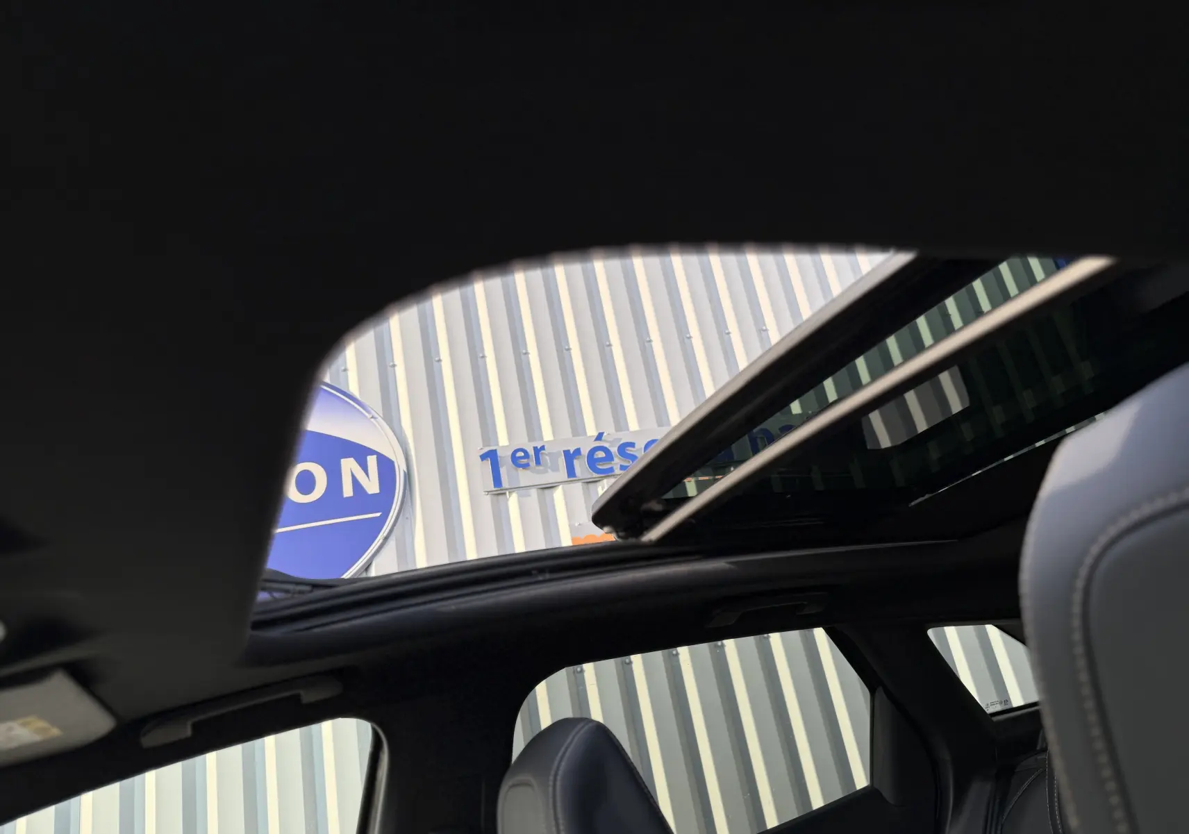 Vue intérieure du toit ouvrant panoramique du Peugeot 3008 gris, mettant en valeur les sièges en cuir et la lumière naturelle.