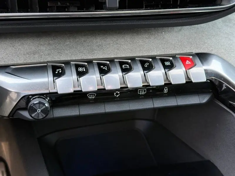 Gros plan sur la rangée de boutons métalliques du tableau de bord du Peugeot 3008 2024, avec bouton d’alerte rouge à droite.