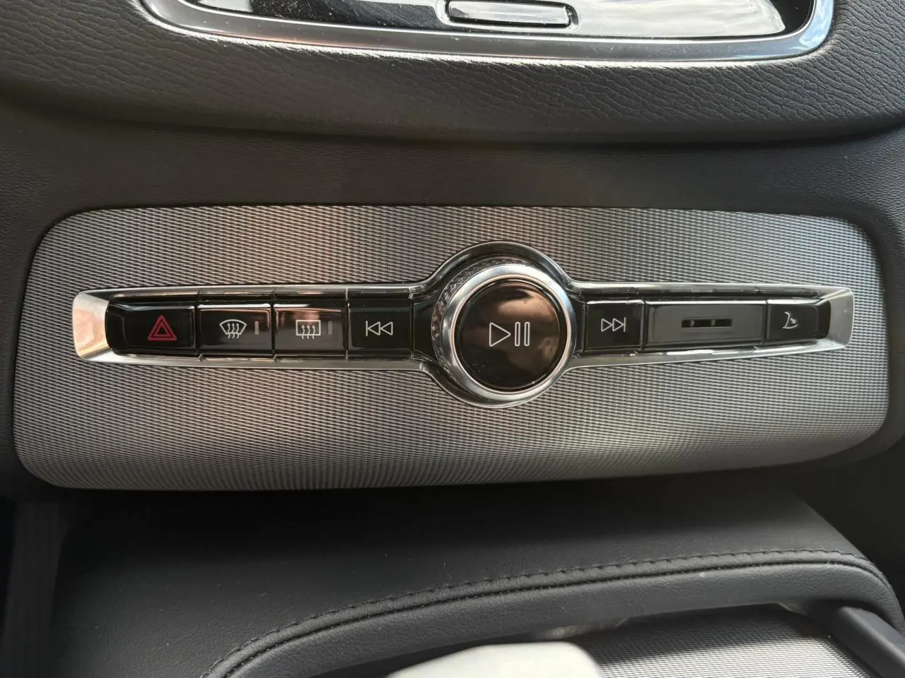 Gros plan sur la commande centrale multimédia chromée du Volvo XC90 T8 gris Dusk, avec boutons de lecture et alertes.