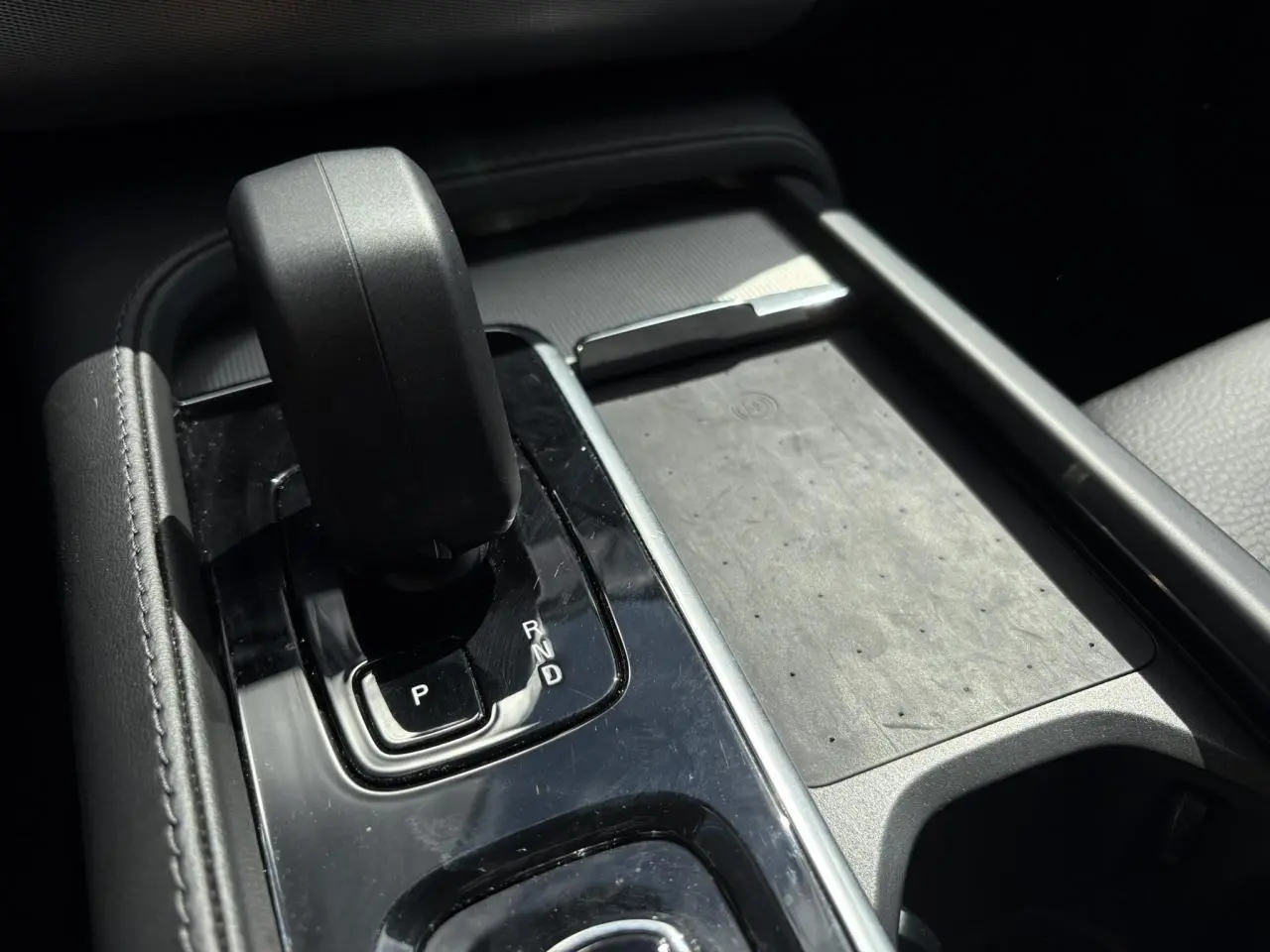 Gros plan sur la console centrale noire du Volvo XC90 T8 hybride, avec levier de vitesses automatique et chargeur à induction.