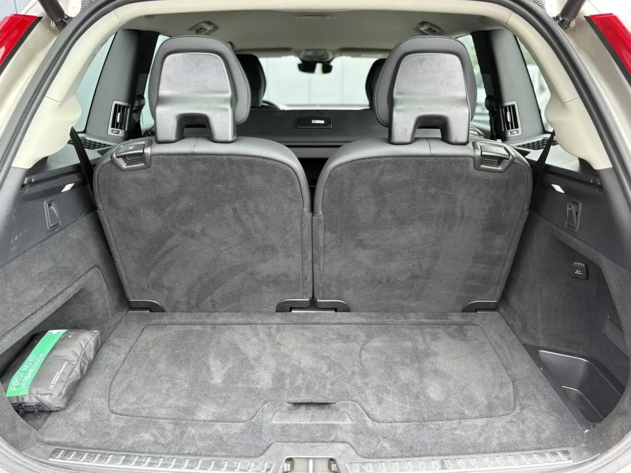 Vue arrière du coffre spacieux d’un Volvo XC90 gris Dusk avec sièges rabattus et kit de premiers secours visible à gauche.