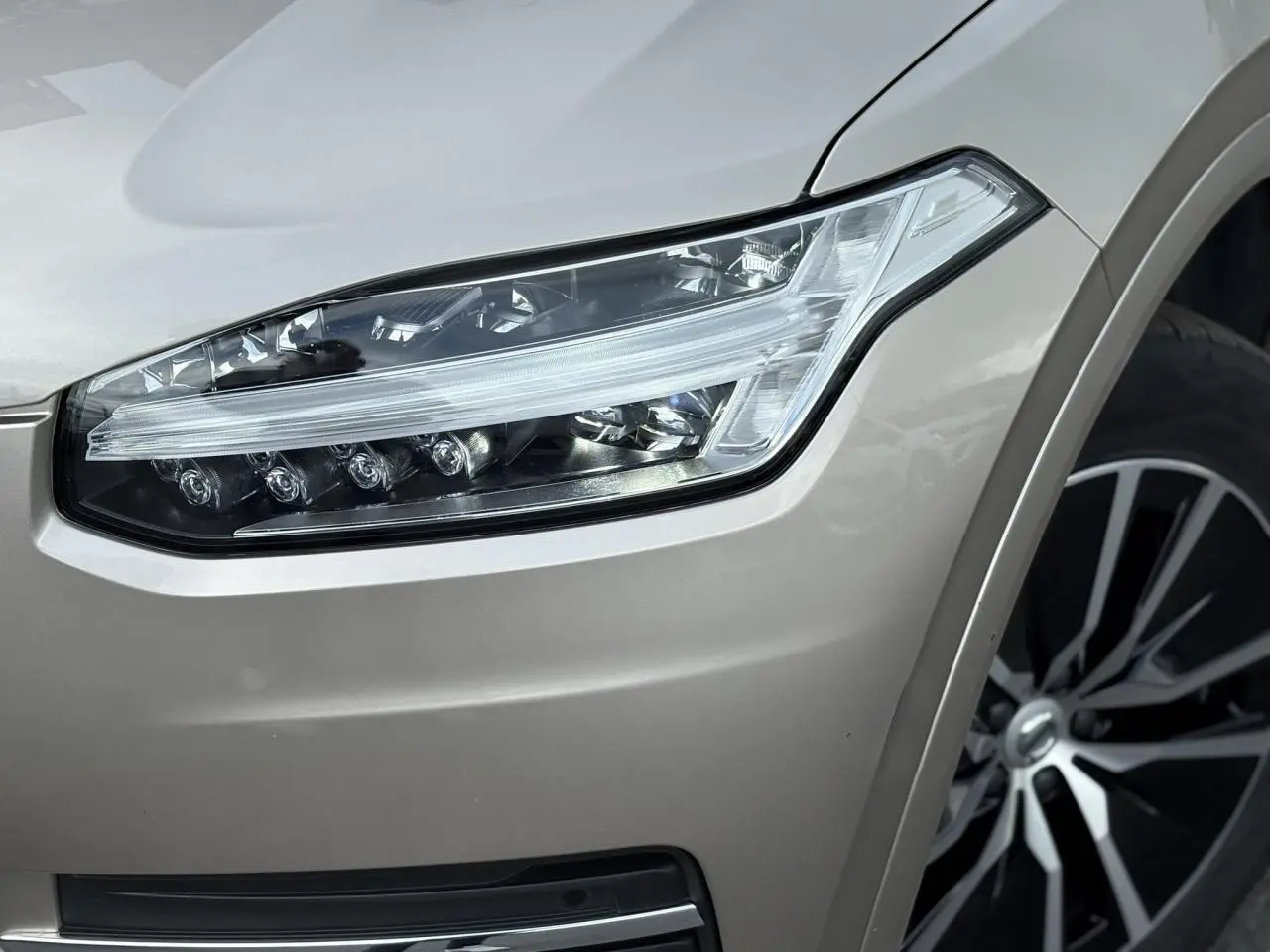 Gros plan sur le phare avant droit et la jante alliage 19 pouces noir diamant du Volvo XC90 gris Dusk.