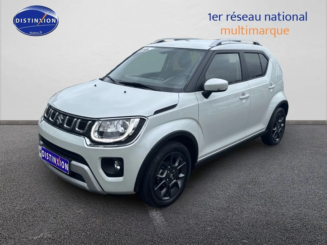Suzuki Ignis blanc perle vue 3/4 avant droit avec jantes noires et barres de toit visibles.