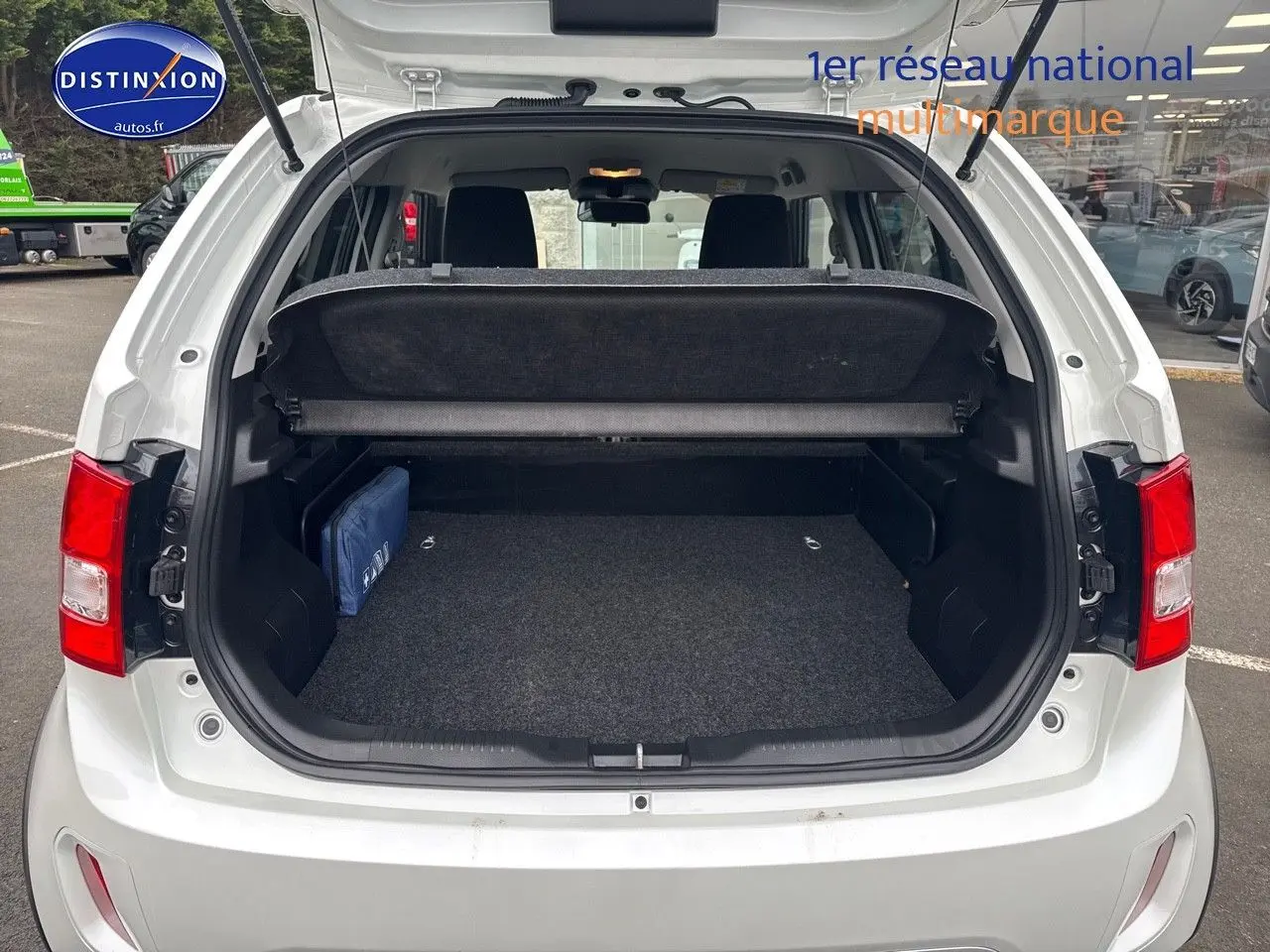 Vue arrière du coffre ouvert d'une Suzuki Ignis 2023 blanche Pure White Pearl métallisé, avec cache-bagages et intérieur noir.