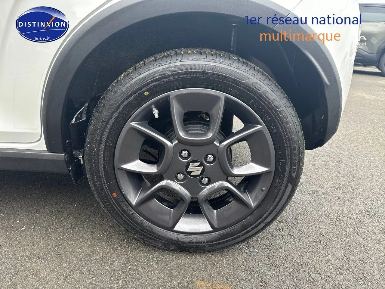 Gros plan sur la roue avant gauche de la Suzuki Ignis 2023 en Pure White Pearl métallisé avec jante alu gris foncé.