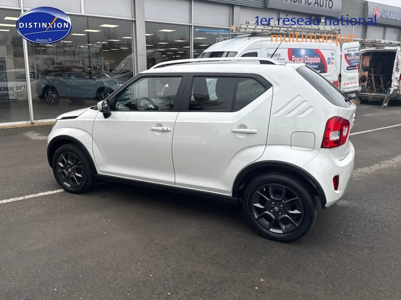 Vue de profil côté gauche d'une Suzuki Ignis blanche nacrée avec jantes noires et barres de toit visibles.