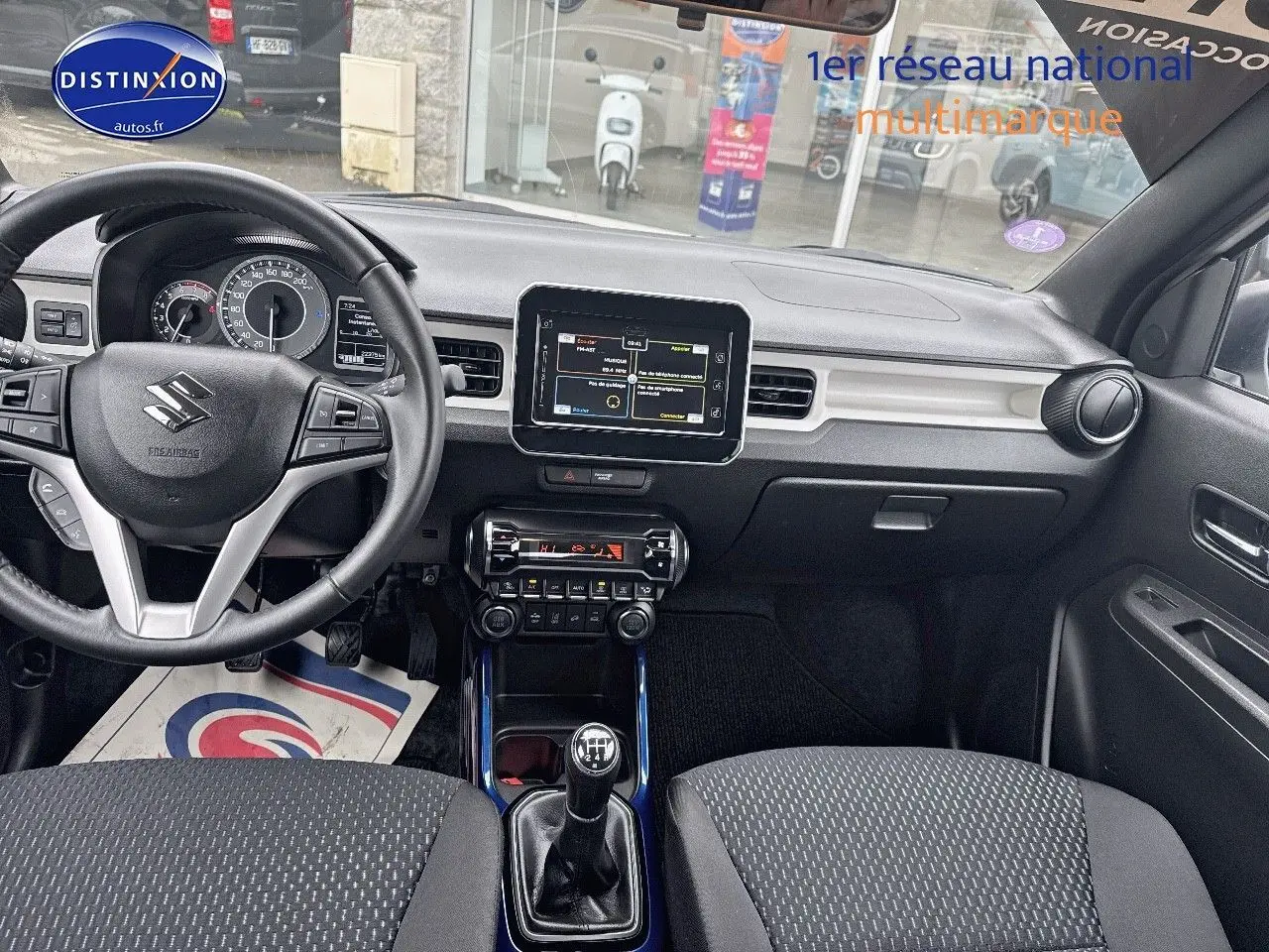 Vue intérieure avant de la Suzuki Ignis 2023 blanche, volant cuir multifonction et écran tactile central visible.
