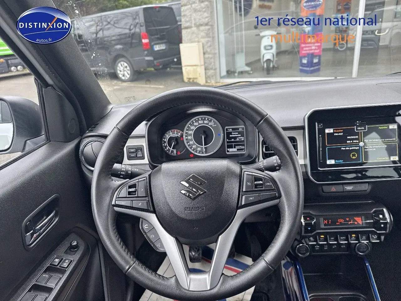 Vue intérieure centrée sur le volant cuir multifonction d'une Suzuki Ignis blanche, avec tableau de bord et écran tactile visibles.