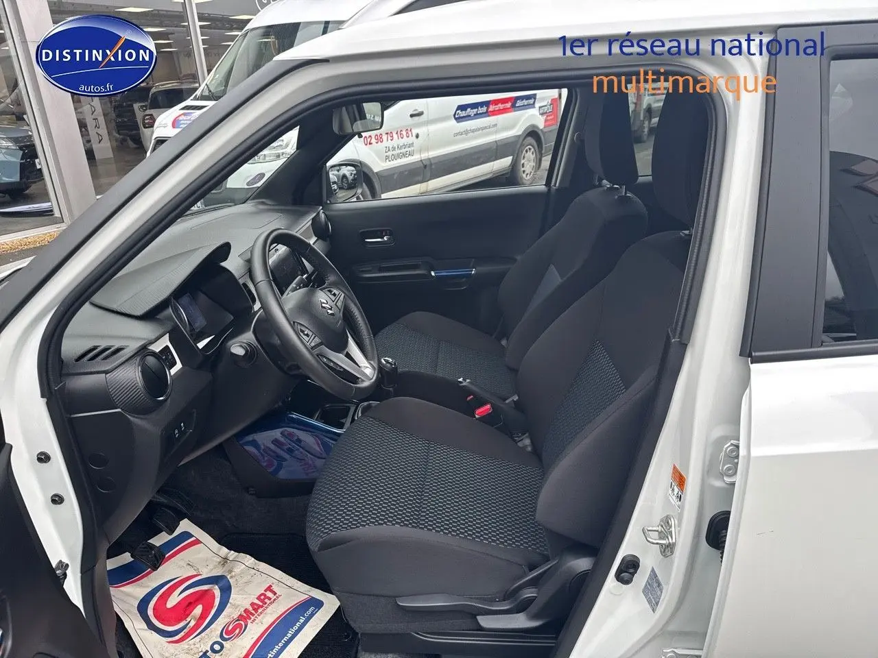 Vue intérieure côté conducteur de la Suzuki Ignis 2023 blanche, montrant sièges et tableau de bord avec volant cuir.