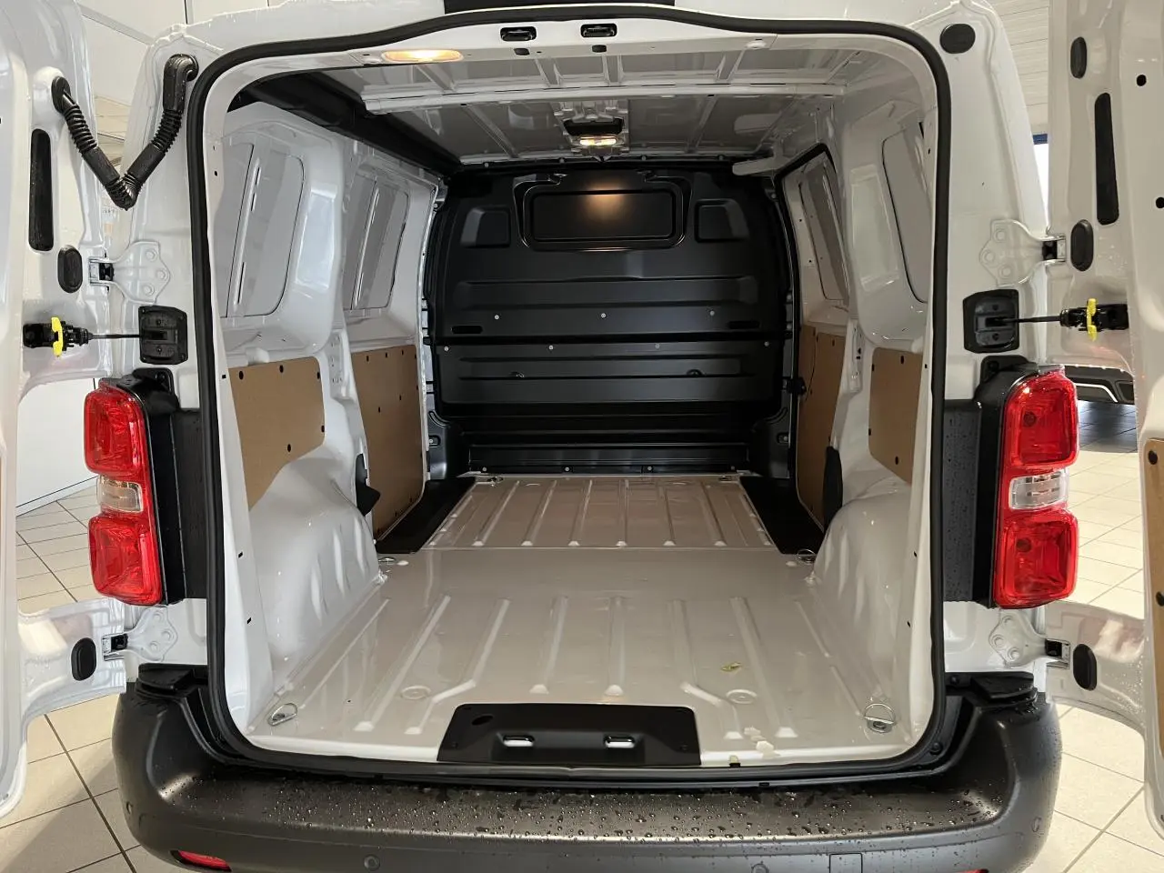 Vue arrière ouverte du Peugeot Expert Fourgon blanc 2024, montrant l'espace de chargement vide avec parois protégées et plancher métallique.
