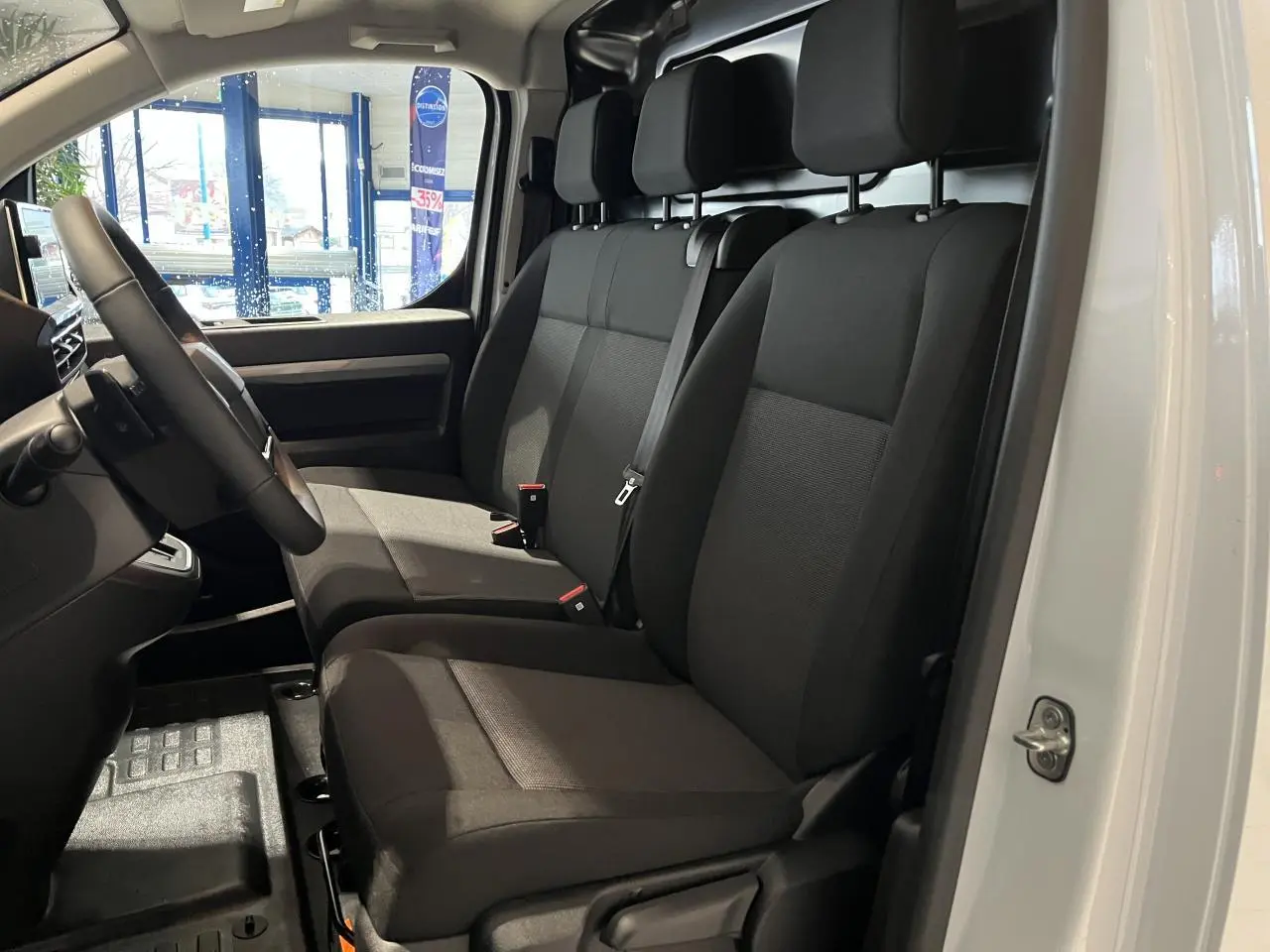 Vue intérieure côté conducteur du Peugeot Expert Fourgon blanc 2024, montrant les sièges tissu bi-ton noir-gris et le volant cuir.