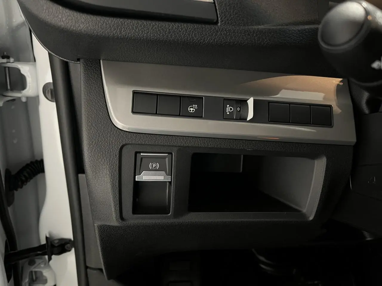 Détail intérieur côté gauche du tableau de bord du Peugeot Expert Fourgon blanc 2024, avec commandes éclairage et frein de stationnement électrique.