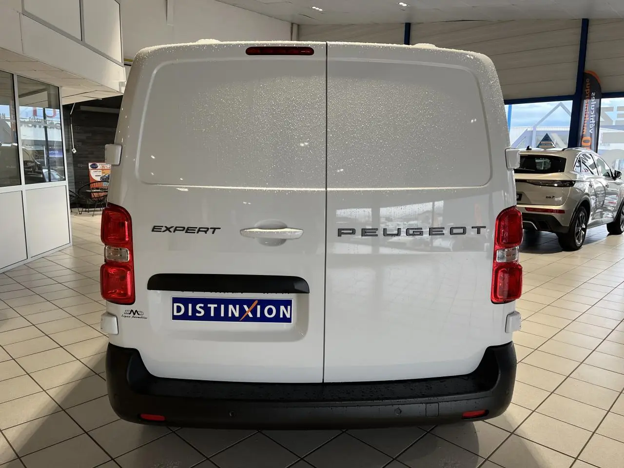 Vue arrière du Peugeot Expert Fourgon blanc 2024 avec portes battantes et feux rouges visibles en intérieur showroom.