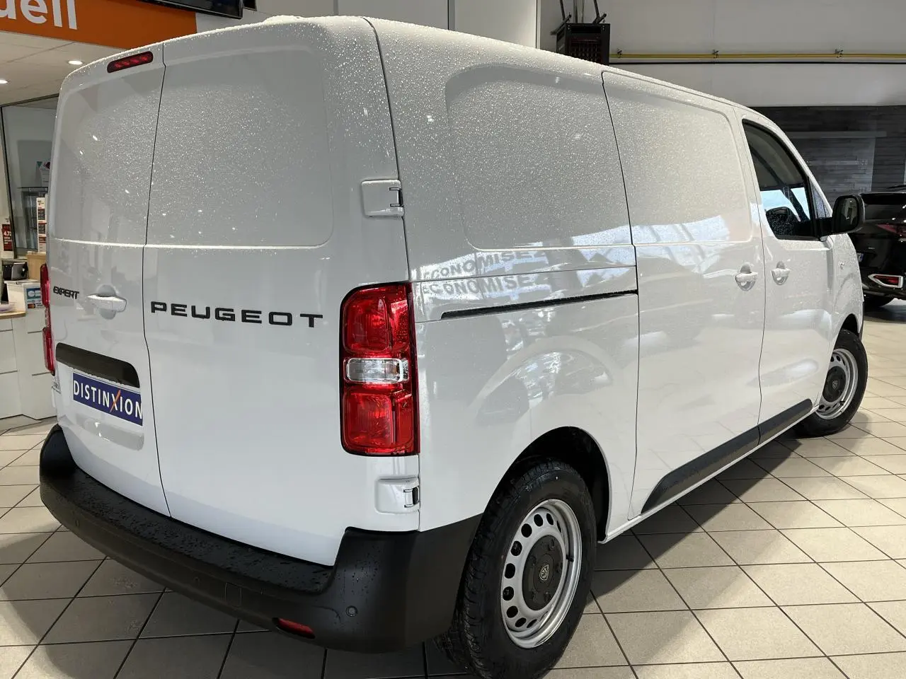 Vue 3/4 arrière droite d’un Peugeot Expert Fourgon blanc 2024 en showroom avec feux arrière rouges et pare-chocs noir.