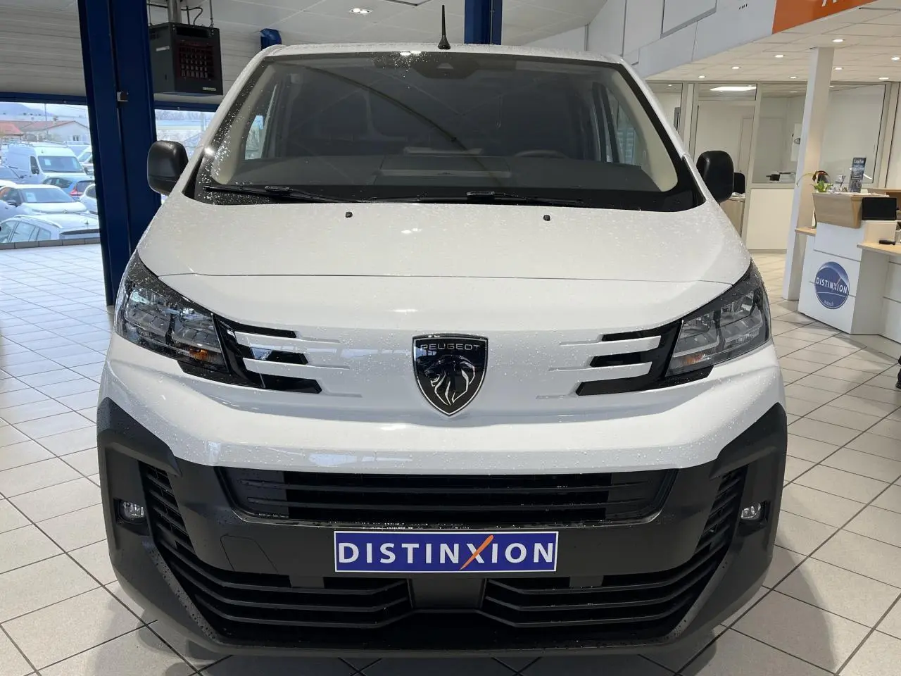 Vue avant du Peugeot Expert Fourgon blanc 2024 avec calandre noire et logo lion central, en intérieur showroom.