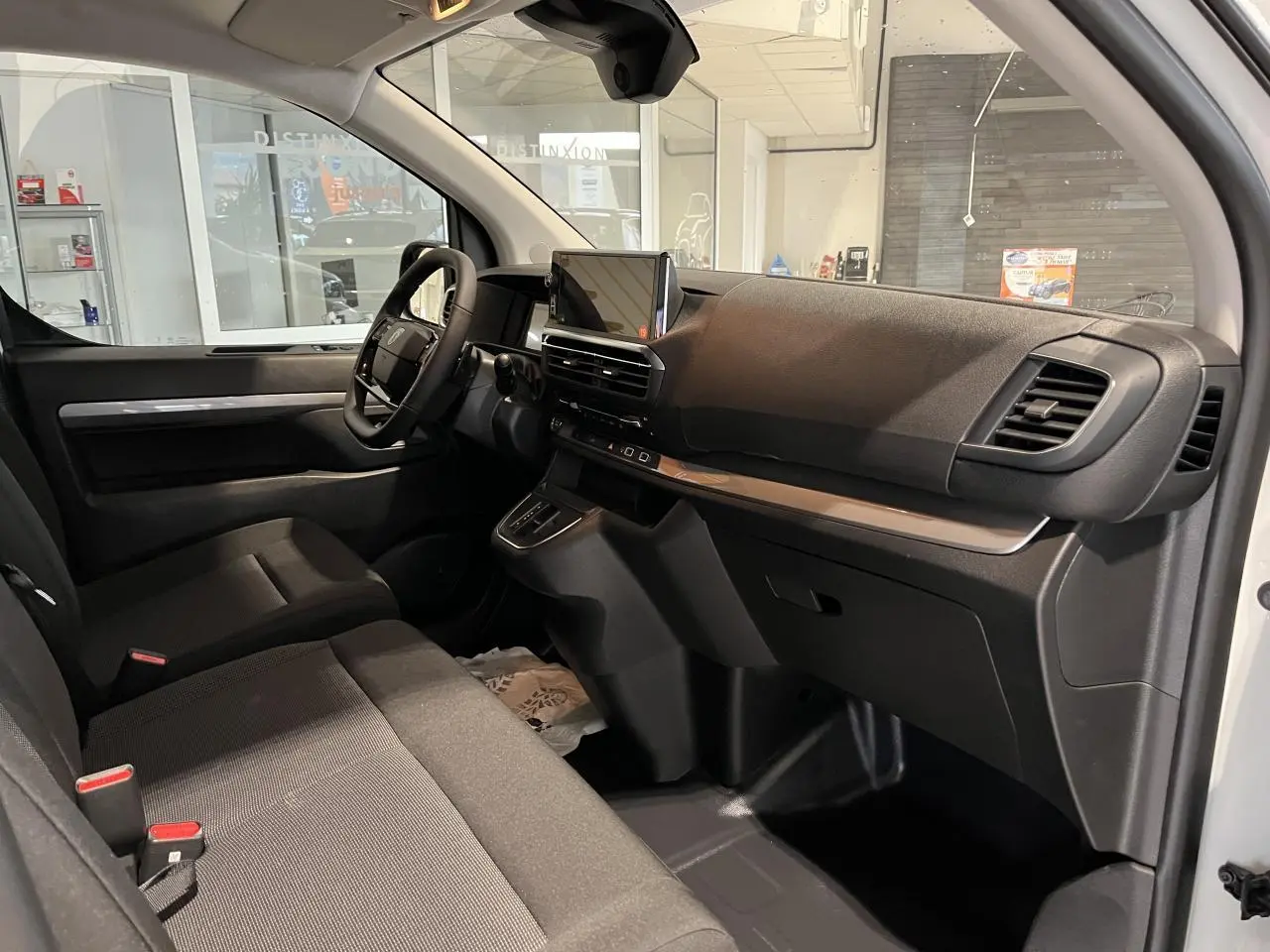 Vue intérieure côté passager du Peugeot Expert Fourgon 2024, montrant la planche de bord noire avec écran tactile et sièges tissu bi-ton noir-gris.