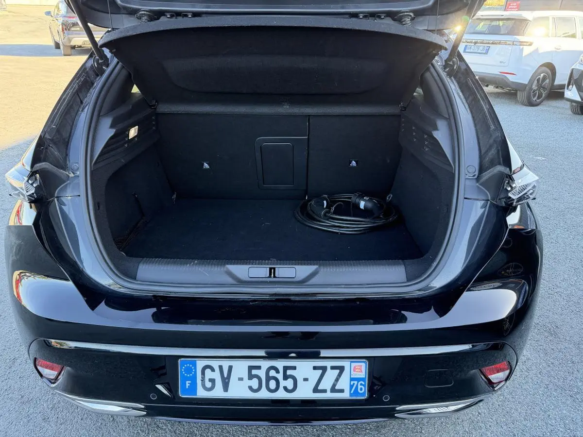 Coffre ouvert d'une Peugeot 308 noire vue de l'arrière, avec câble de recharge visible dans le coffre.