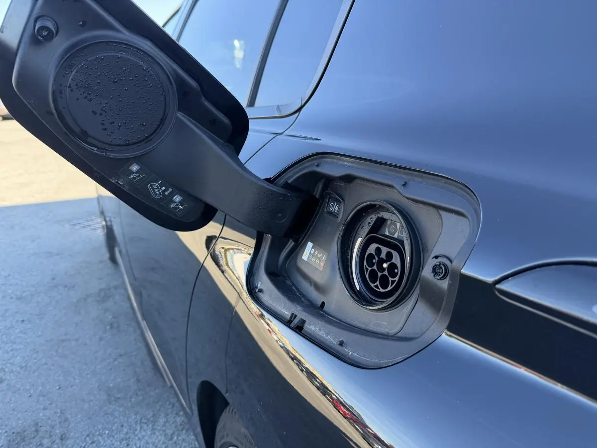 Prise de recharge ouverte côté gauche d’une Peugeot 308 noire métallisée, avec reflets sur la carrosserie.
