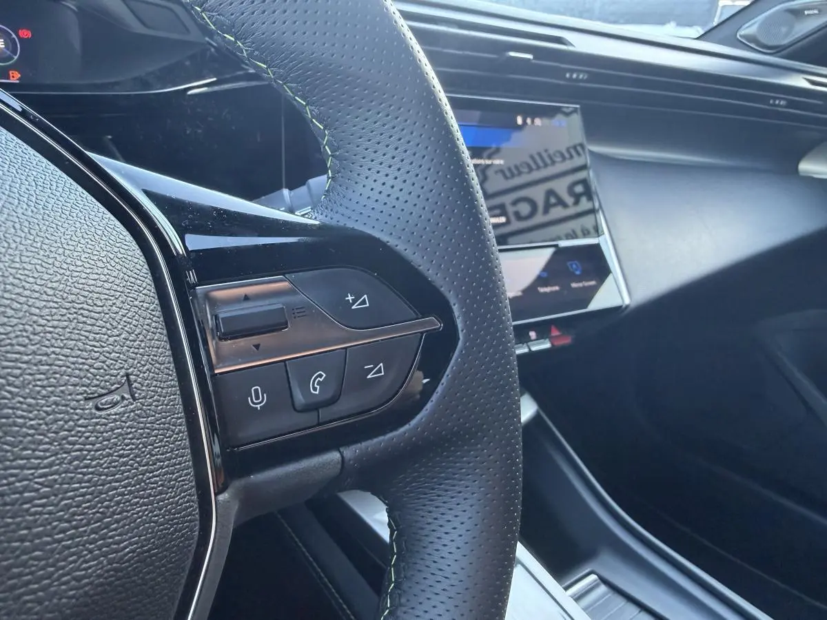 Gros plan sur le volant noir perforé avec surpiqûres vertes et écran tactile du tableau de bord de la Peugeot 308 2024.