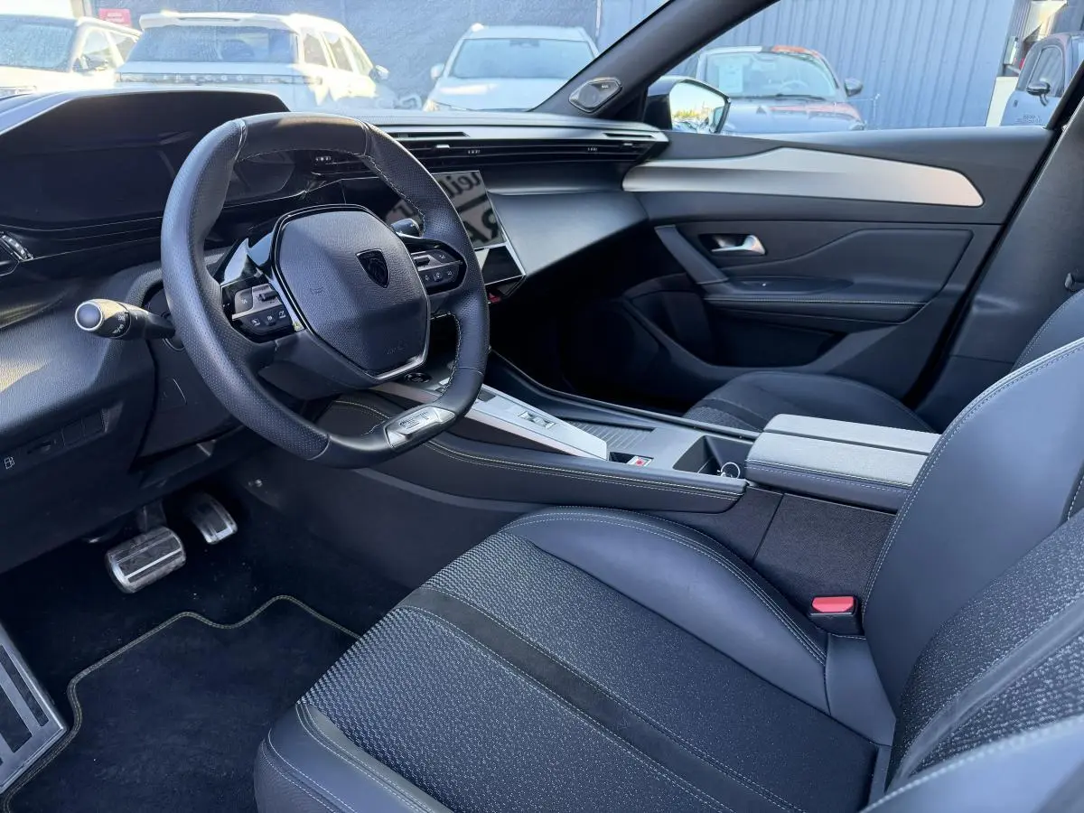 Intérieur avant droit de Peugeot 308 2024 noir, volant compact, sellerie mixte tissu/TEP et console centrale moderne.