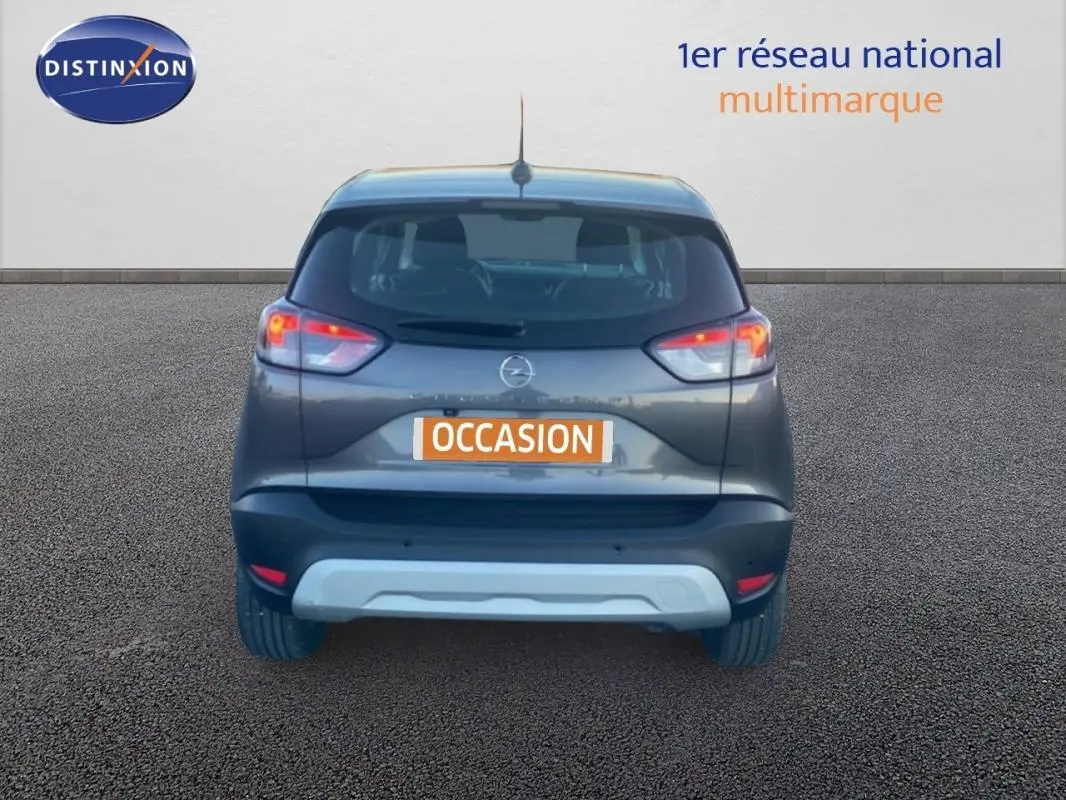 Vue arrière d'un Opel Crossland gris foncé 2022 avec feux allumés sur fond neutre.