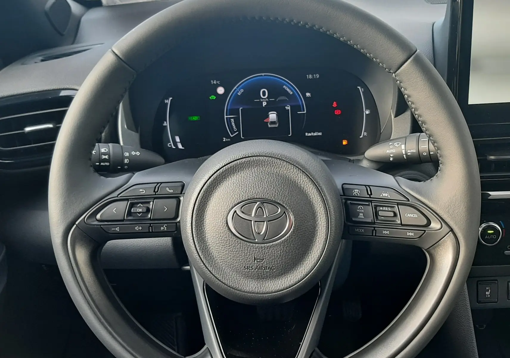 Vue centrée sur le volant noir de la Toyota Yaris Cross 130H Design 2025 avec tableau de bord numérique allumé.