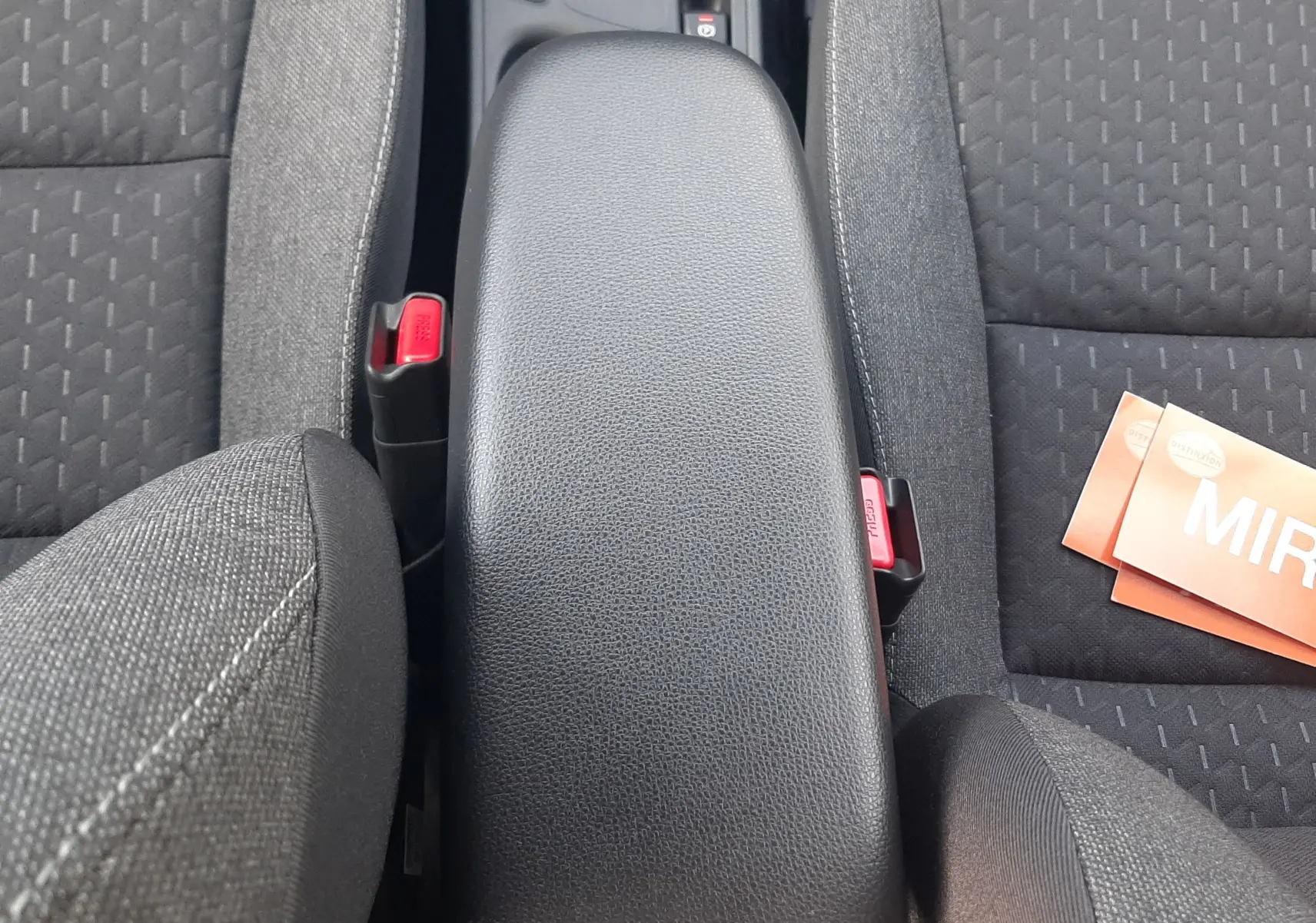 Vue plongeante sur l'accoudoir central noir et les sièges en tissu gris foncé de la Toyota Yaris Cross 130H Design 2025.