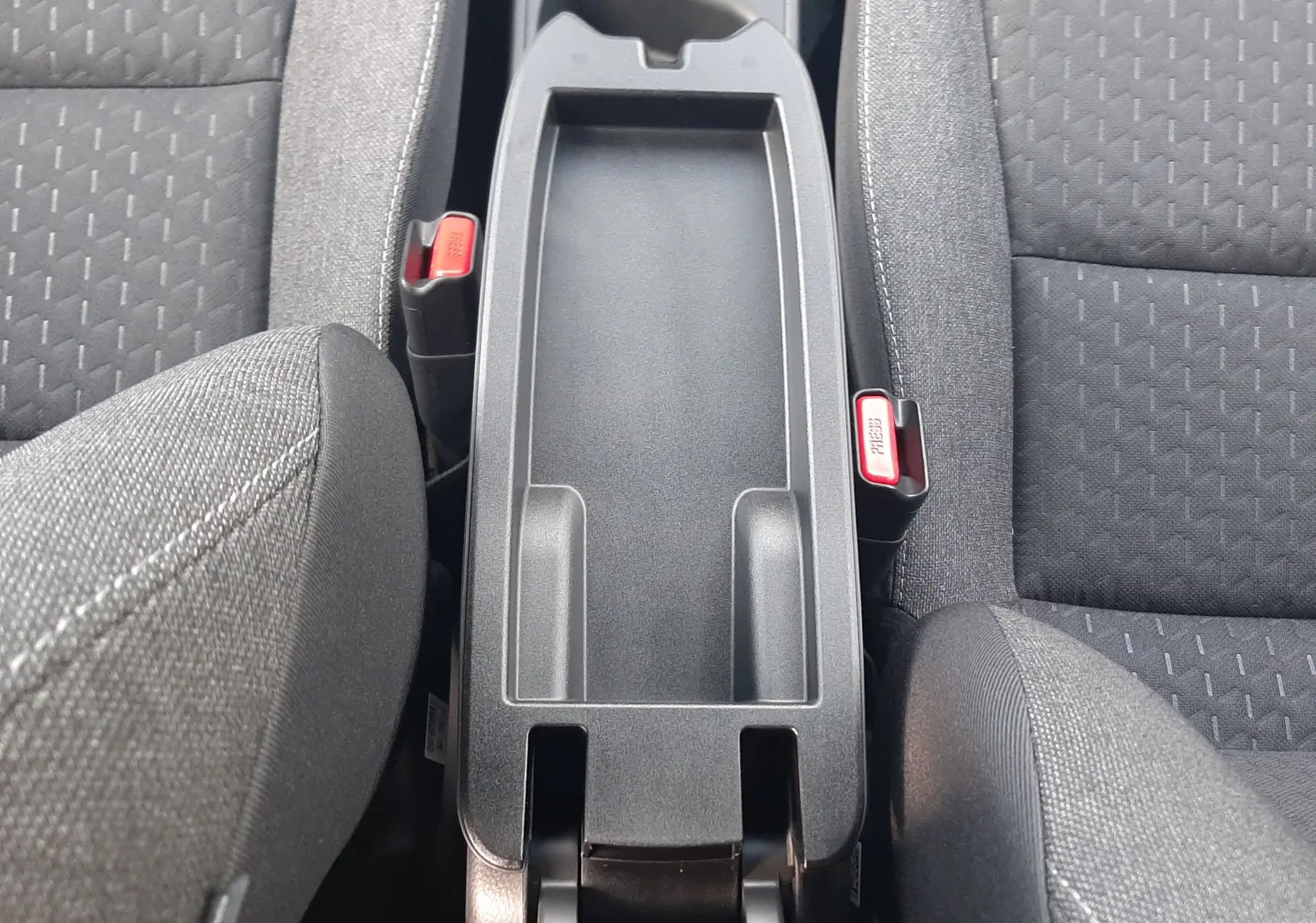 Vue plongeante sur la console centrale noire entre les sièges tissu gris de la Toyota Yaris Cross 130H Design 2025.
