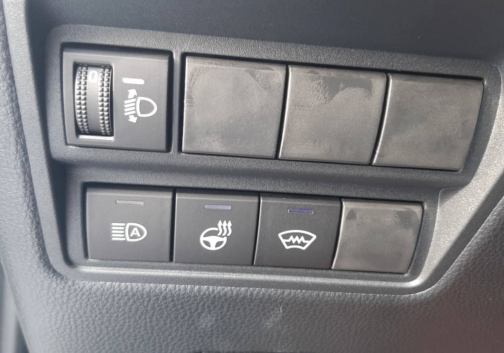 Panneau de commandes noires avec réglage des phares, chauffage de volant et dégivrage sur Toyota Yaris Cross 130H gris minéral.