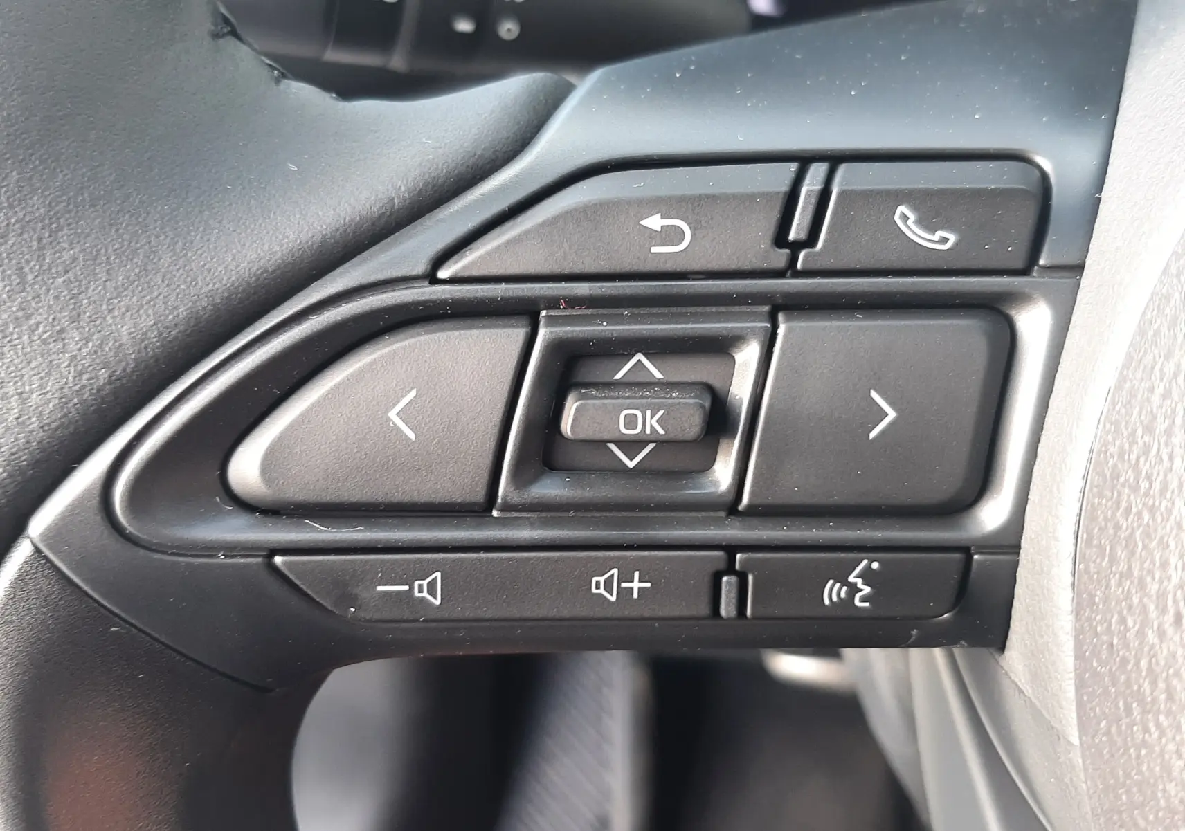 Gros plan sur les commandes multifonctions côté gauche du volant de la Toyota Yaris Cross 130H Design gris minéral 2025.