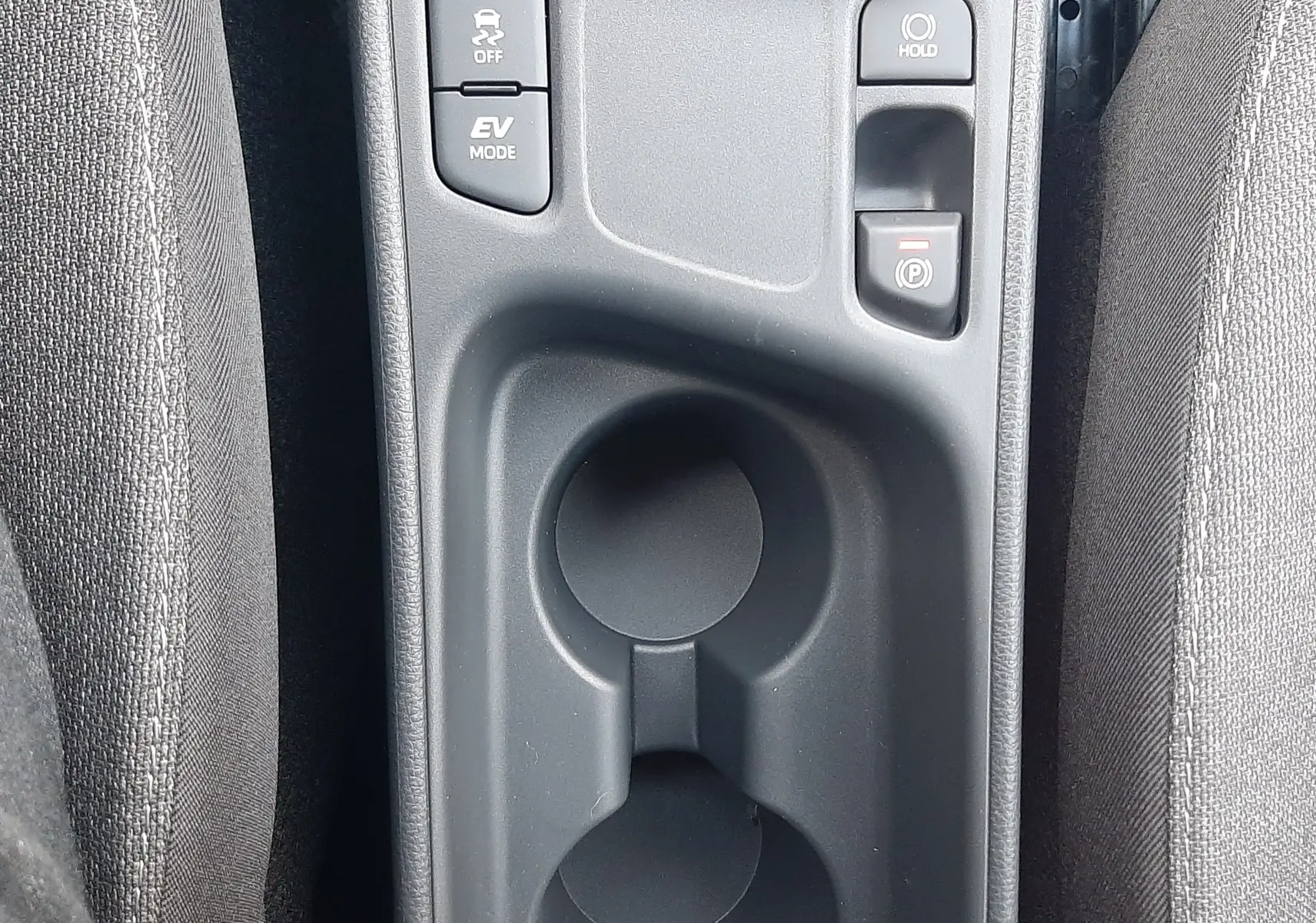 Vue rapprochée de la console centrale grise avec porte-gobelets et boutons de modes de conduite dans une Toyota Yaris Cross 130H Design 2025.