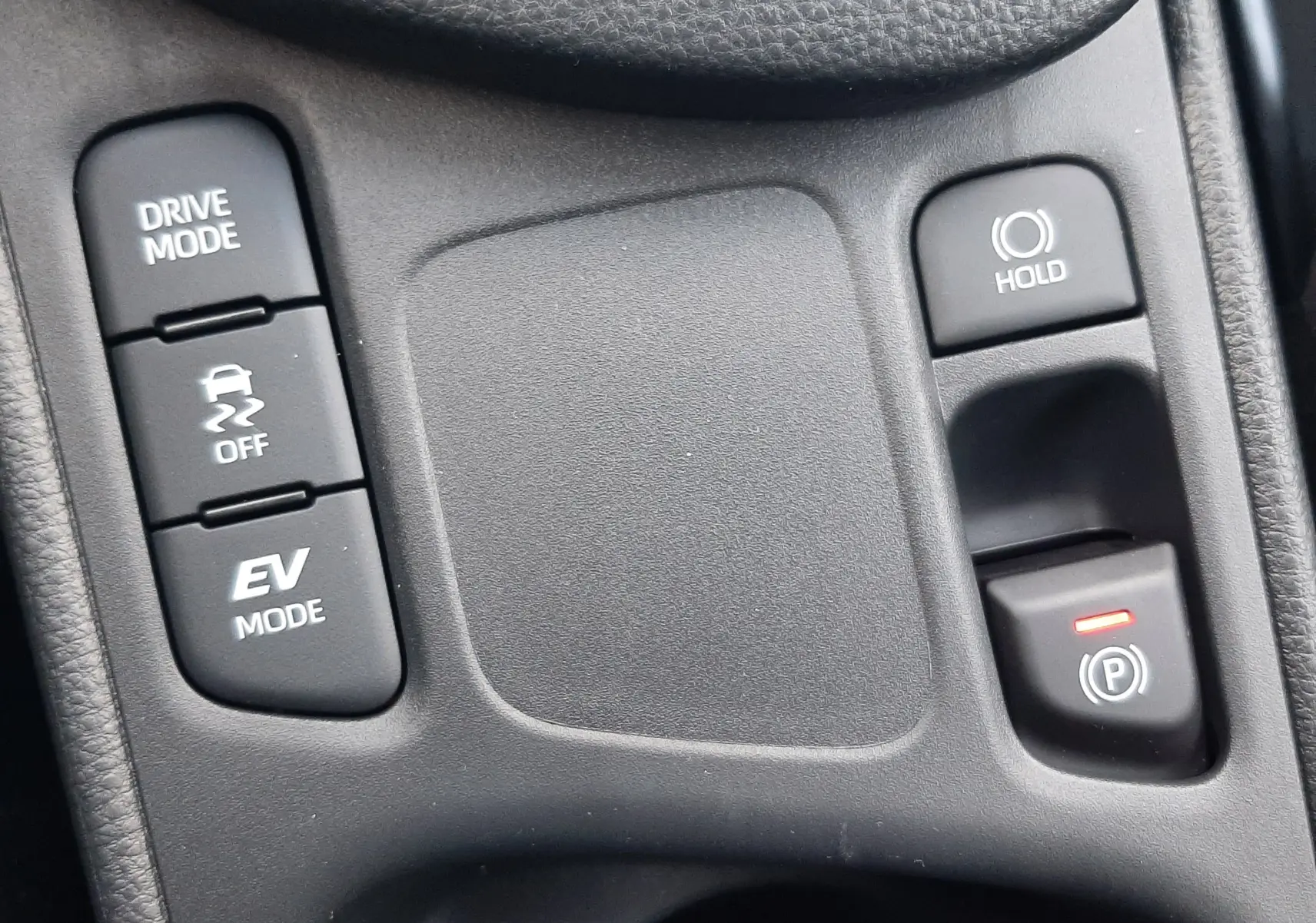 Gros plan sur les commandes centrales noires de la Toyota Yaris Cross 130H Design, avec boutons Drive Mode, EV Mode et frein à main électronique.