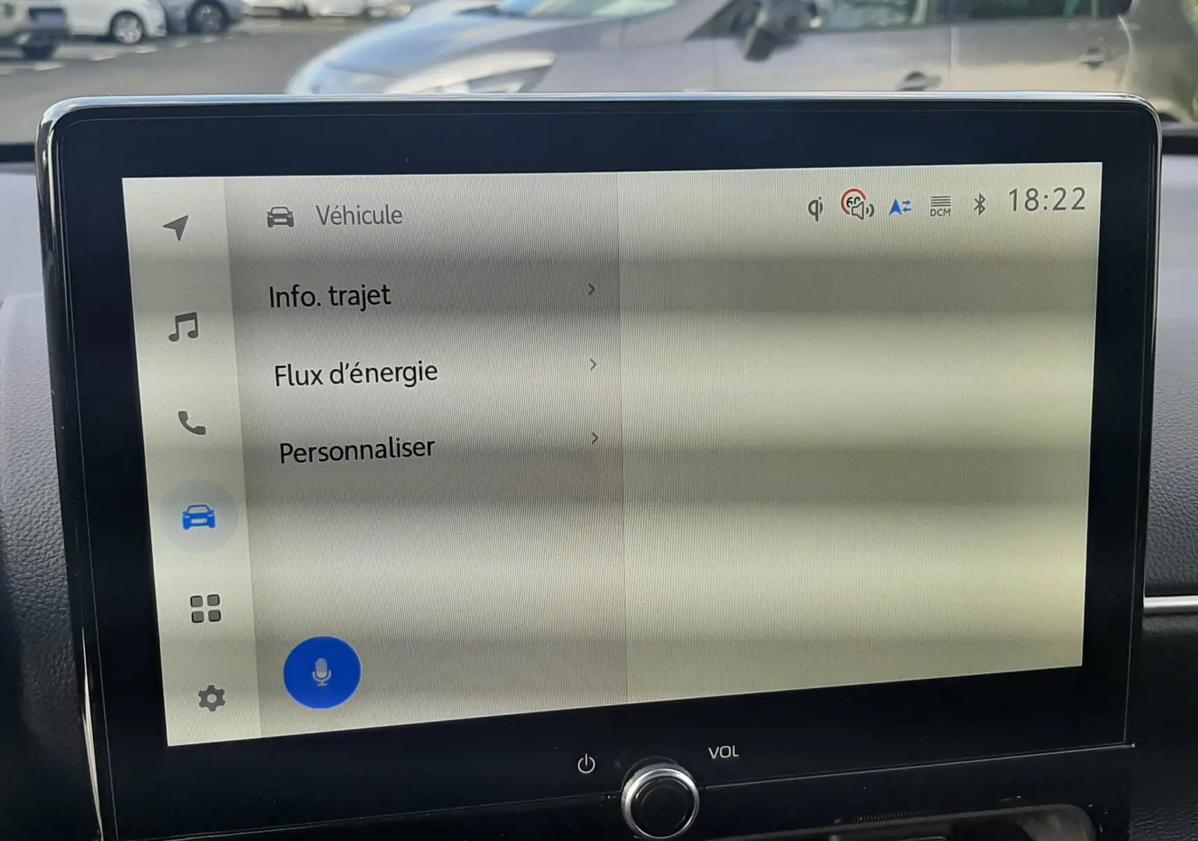 Écran tactile central de la Toyota Yaris Cross 130H Design affichant les options véhicule, avec vue floue sur un extérieur urbain.