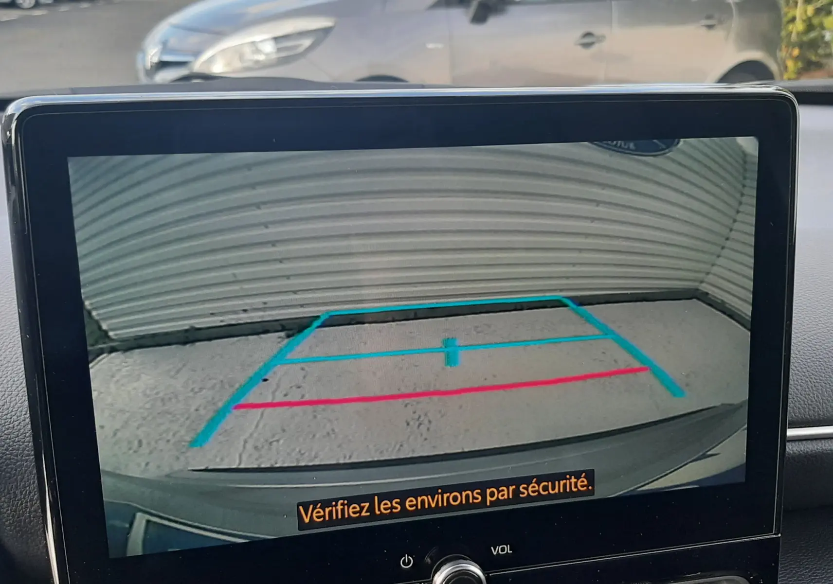Écran de caméra de recul affichant les lignes de guidage bleues et rouges sur fond gris, tableau de bord d'une Toyota Yaris Cross 130H Design.