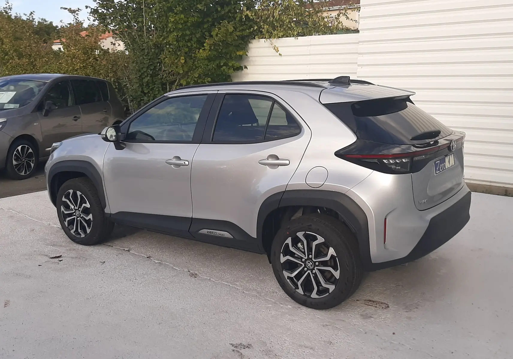 Vue 3/4 arrière droite d'une Toyota Yaris Cross 130H Design gris minéral avec jantes bicolores et toit noir.