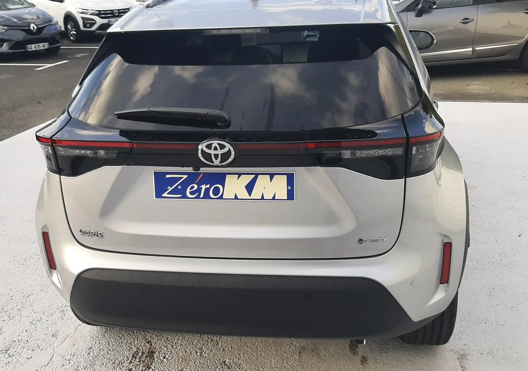 Vue arrière d'une Toyota Yaris Cross 130H Design gris minéral avec feux reliés par une bande noire et logo Toyota visible.