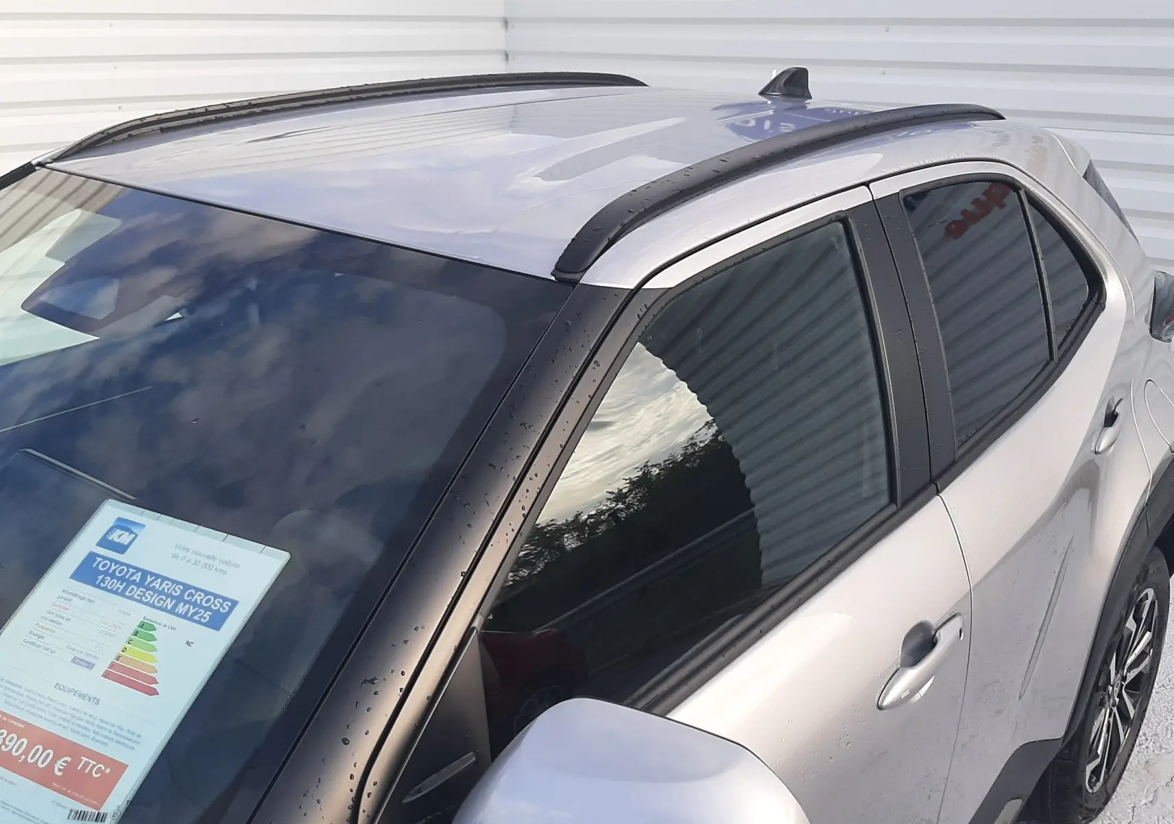 Toyota Yaris Cross 130H Design gris minéral vue 3/4 avant droit avec barres de toit et rétroviseur argenté.